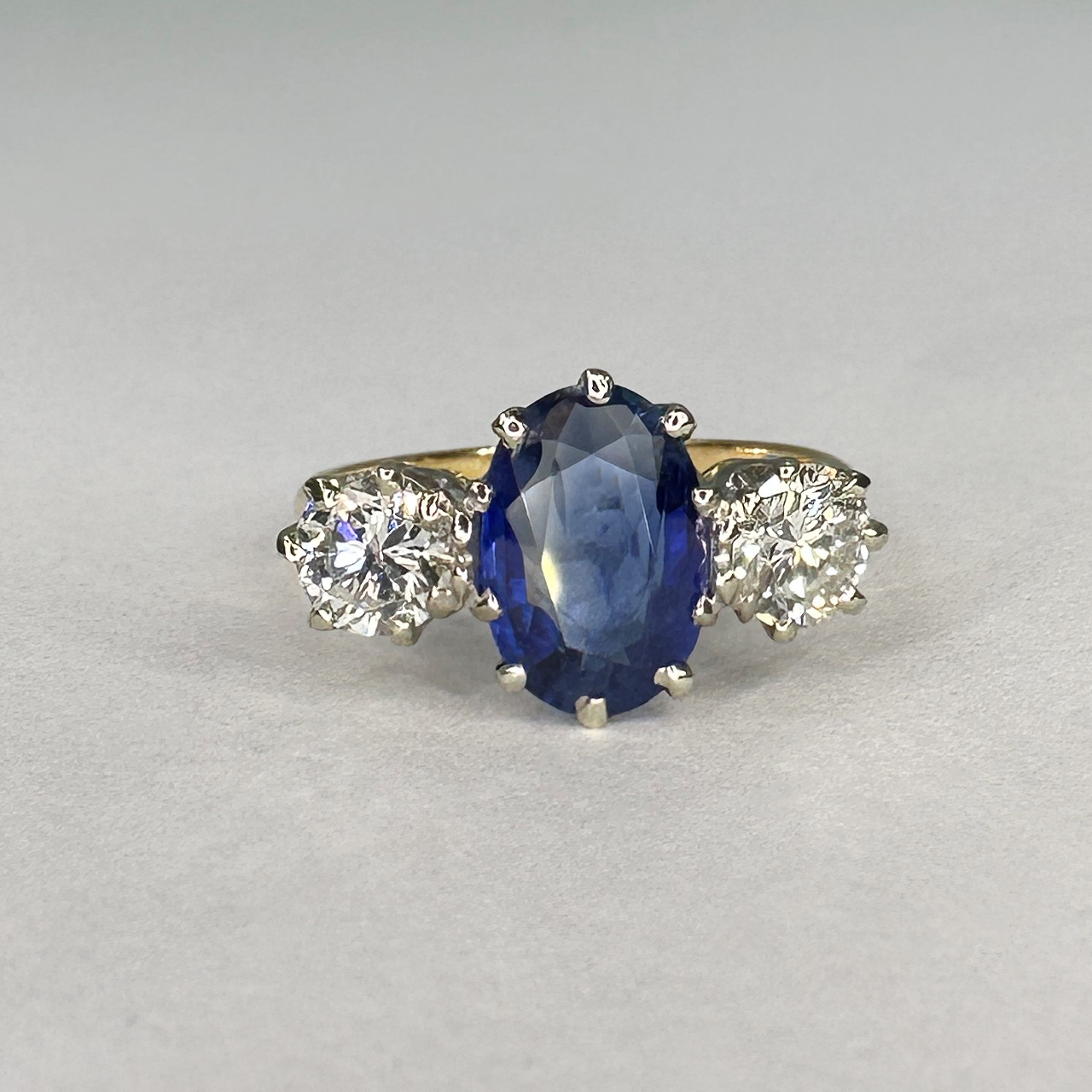Exquisite Ceylon Blue Sapphire Ring. The central oval sapphire is a typical mid to light blue. The 1.8 ct weight sapphire has a few natural inclusions and is nestled between two sparkling, bright 0.5ct brilliant cut diamonds, total weight of diamonds 1 ct.The ring is claw set in 18ct white gold, the shank is in 18ct yellow gold. Please contact us for more information, photos or a video.This stunning ring can be resized.