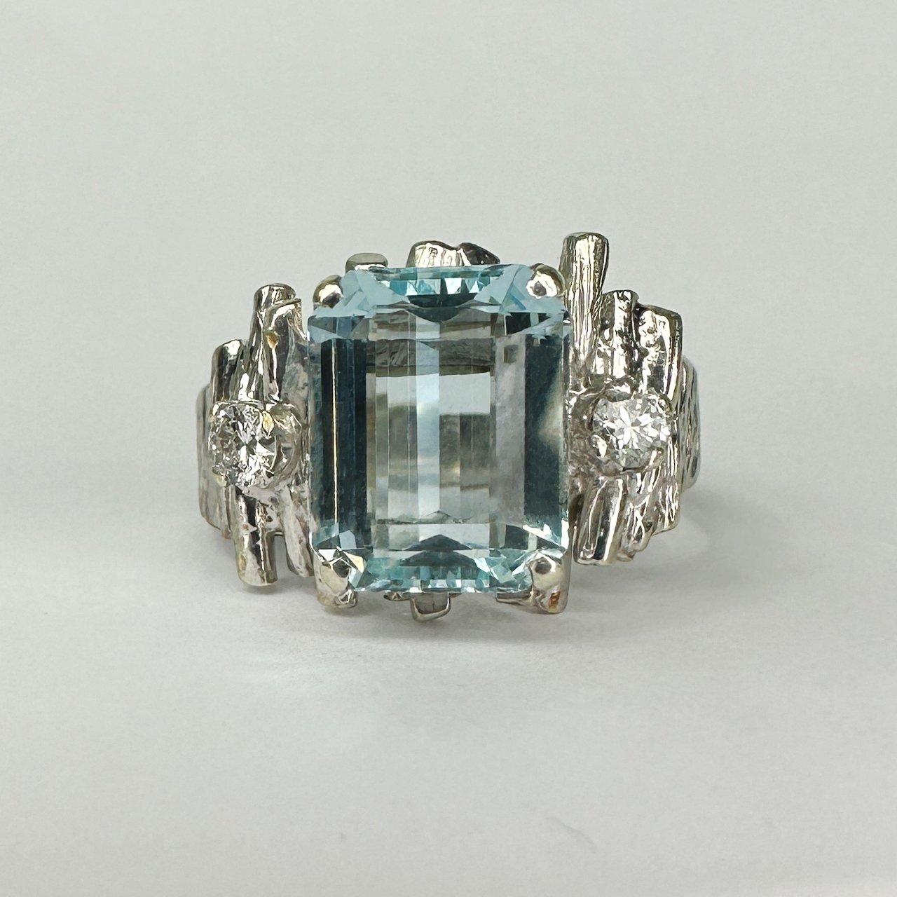 Aquamarine and Diamond Bark Textured White Gold Ring. 1970's bark construction with a beautiful aquamarine centre stone measuring 10mm long x 8mm wide x 5mm deep, flanked on either side by 2 bright brilliant cut diamonds . The ring looks amazing on the finger and comfortable to wear. All stones are claw set. A fantastic vintage ring with style factor. The ring can be resized, contact us for further information or chat about this lovely ring.